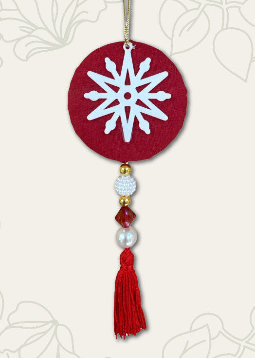 Decorative ornament with snowflake design on a red circle, featuring beads and a tassel against a white background.